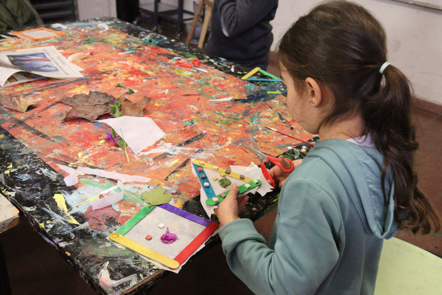 A girl makes colorful geometric figures with paper, scissors, paper and tree leaves.